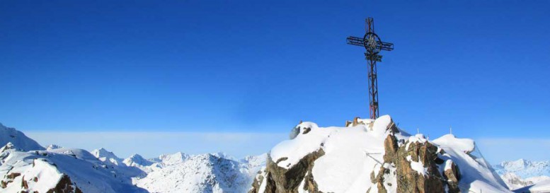 Christian cross on snow covered mountain peak.